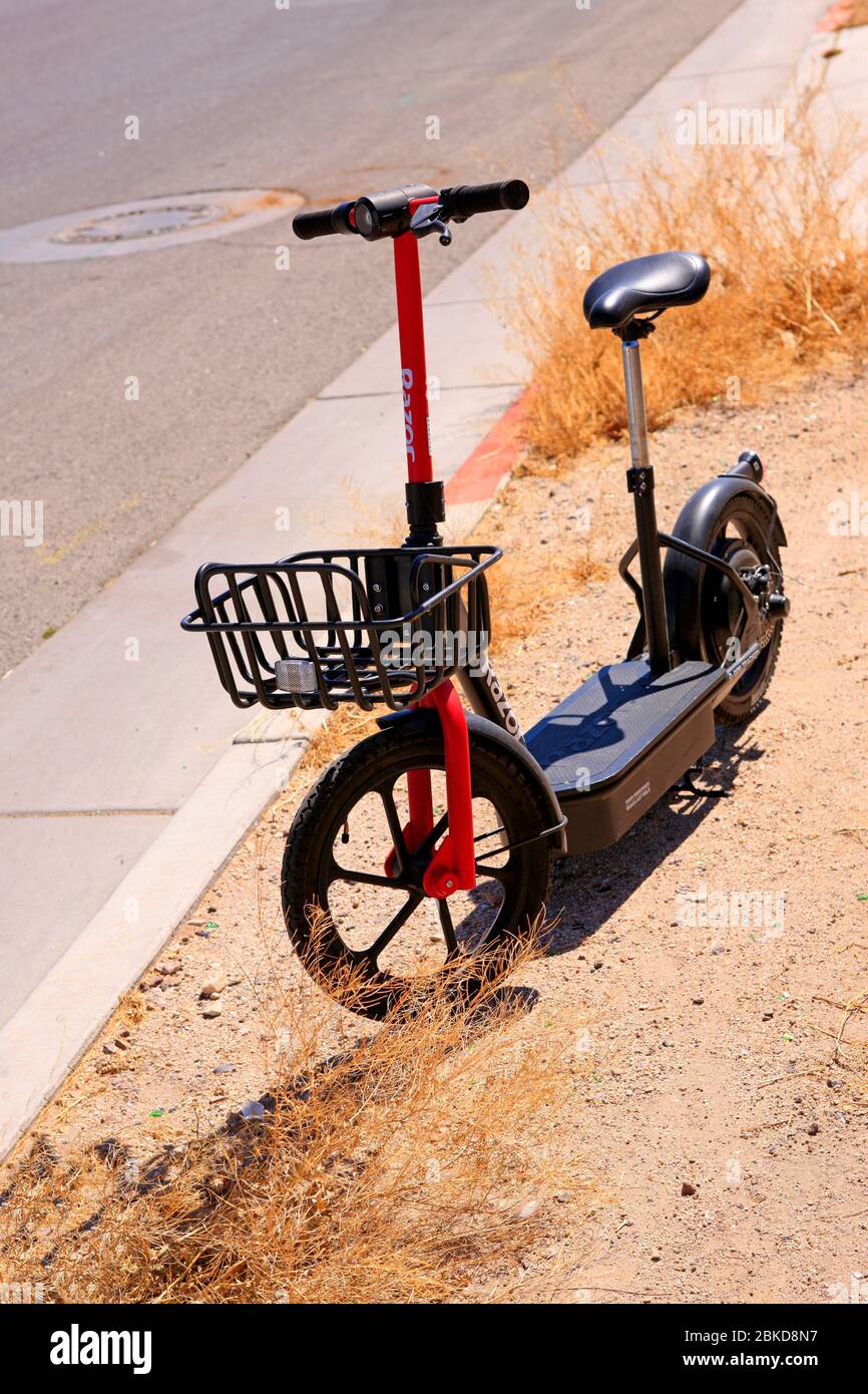 Uno scooter elettrico abbandonato siede tra le erbacce e la polvere in una città vuota di Tucson durante la chiusura a chiave di Covid-19 Foto Stock