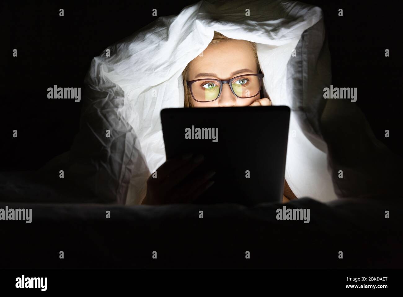 Donna in occhiali che si trovano a letto sotto la coperta utilizzando tablet a tarda notte, non può dormire, addict notizie su Covid-19 o scorrimento social network. Poll Foto Stock