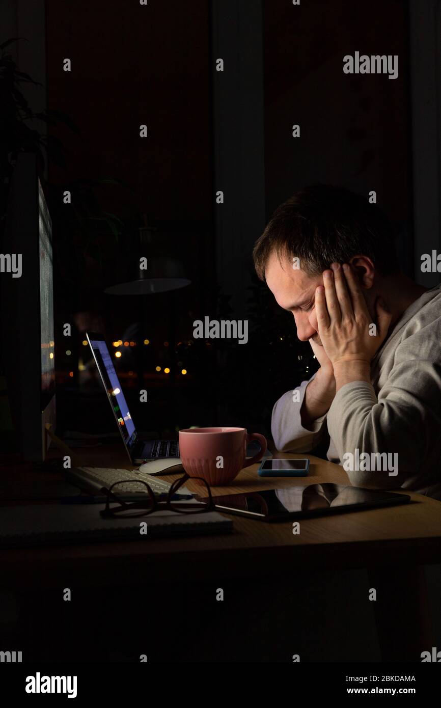 Stanco, sfinito, uomo freelance seduto a un PC desktop / notebook a tarda notte, si addormenta dalla fatica, portando il lavoro a casa durante l'isolamento. Foto Stock