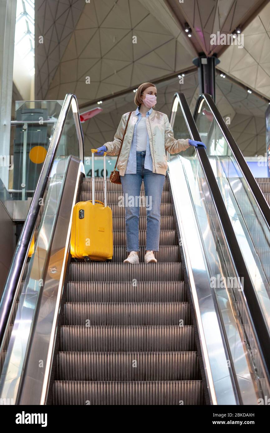 Donna con bagagli gialli si trova sulla scala mobile presso il terminal dell'aeroporto quasi vuoto a causa di restrizioni di viaggio per l'epidemia di coronavirus/Covid-19. Quar Foto Stock