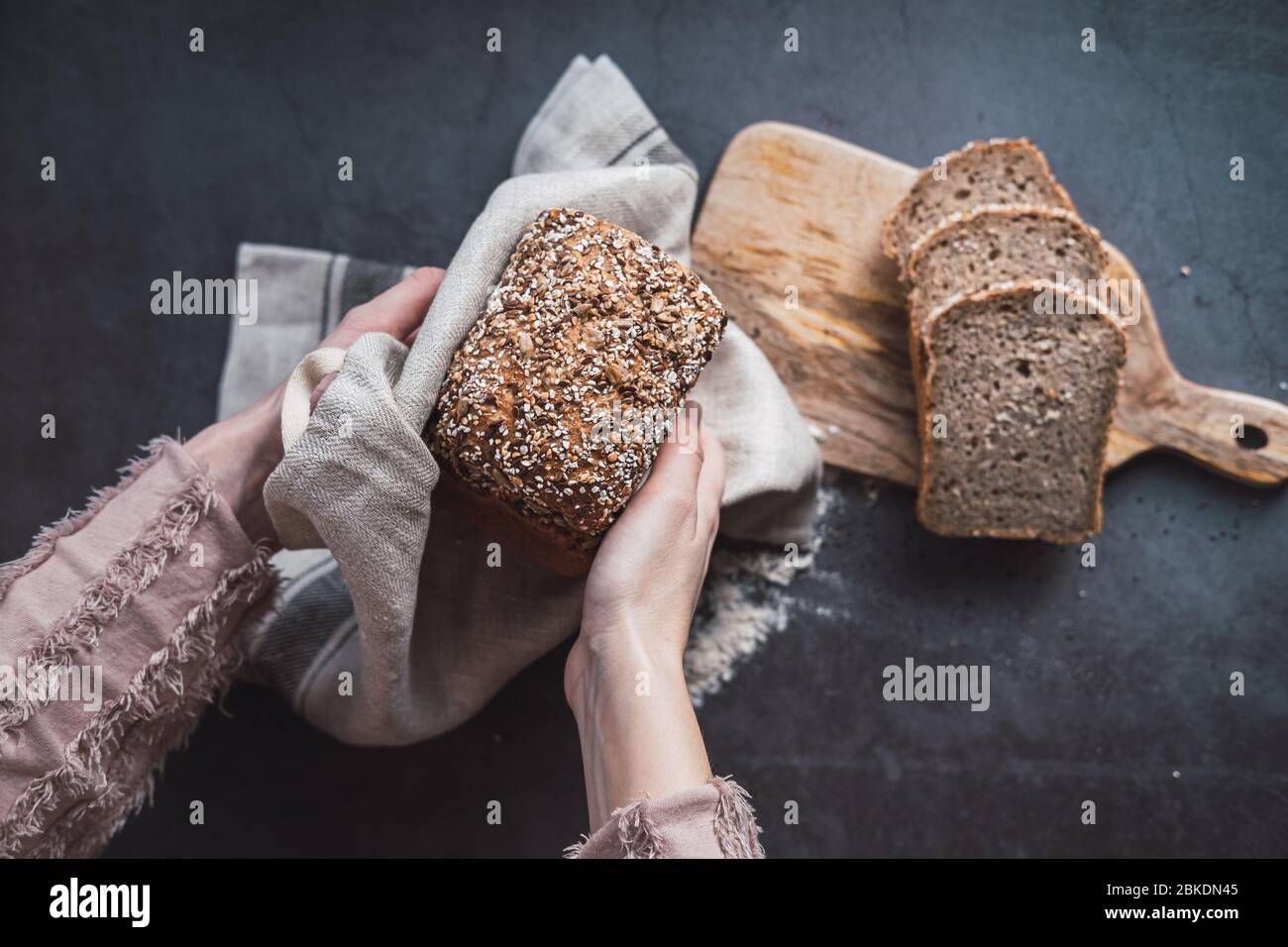 Mani della donna che tengono un pane di grano saraceno con semi di girasole. Foto Stock