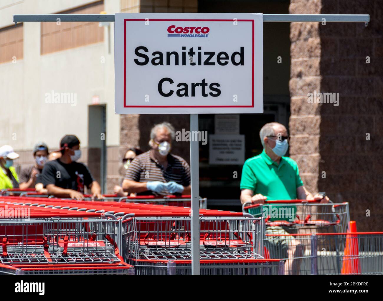 COVID-19 pandemic forza cambiamenti nello shopping: Un cartello indirizza gli acquirenti a carrelli sanitizzati, e gli acquirenti che indossano maschere facciali aspettano di entrare nel negozio. Foto Stock