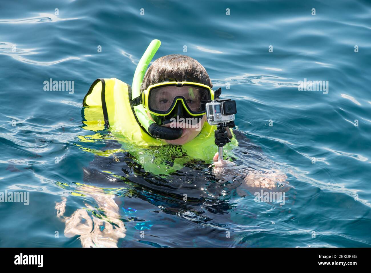 Adolescente caucasico con attrezzatura da snorkeling, tenendo una macchina fotografica subacquea, venendo in su per l'aria da acqua molto blu dei Caraibi. Foto Stock
