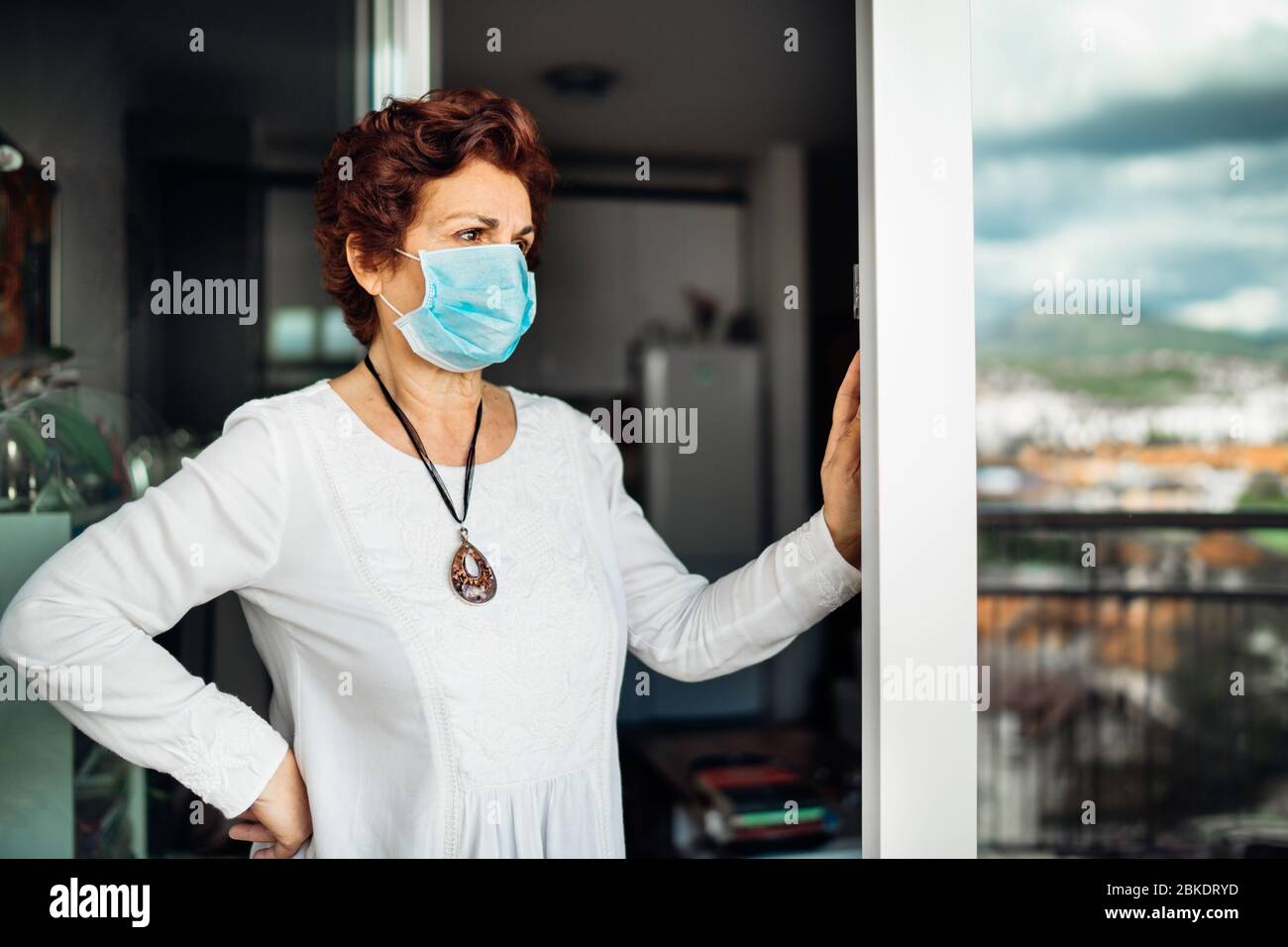 Anziani anziani donna triste a casa, indossare maschera sul balcone window.Coronavirus COVID-19 malattia epidemia infezione Risk.Lockdown socializzazione restrictio Foto Stock