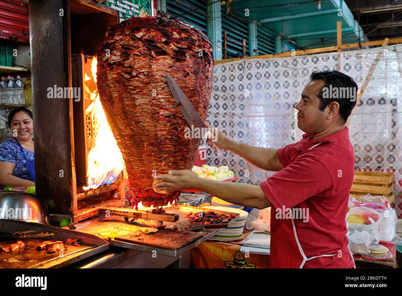 Cameriere che taglia porzioni di carne da un grande shawarma che sta cucinando sopra un fuoco in un ristorante di strada nel mercato comunale di Merida. Foto Stock
