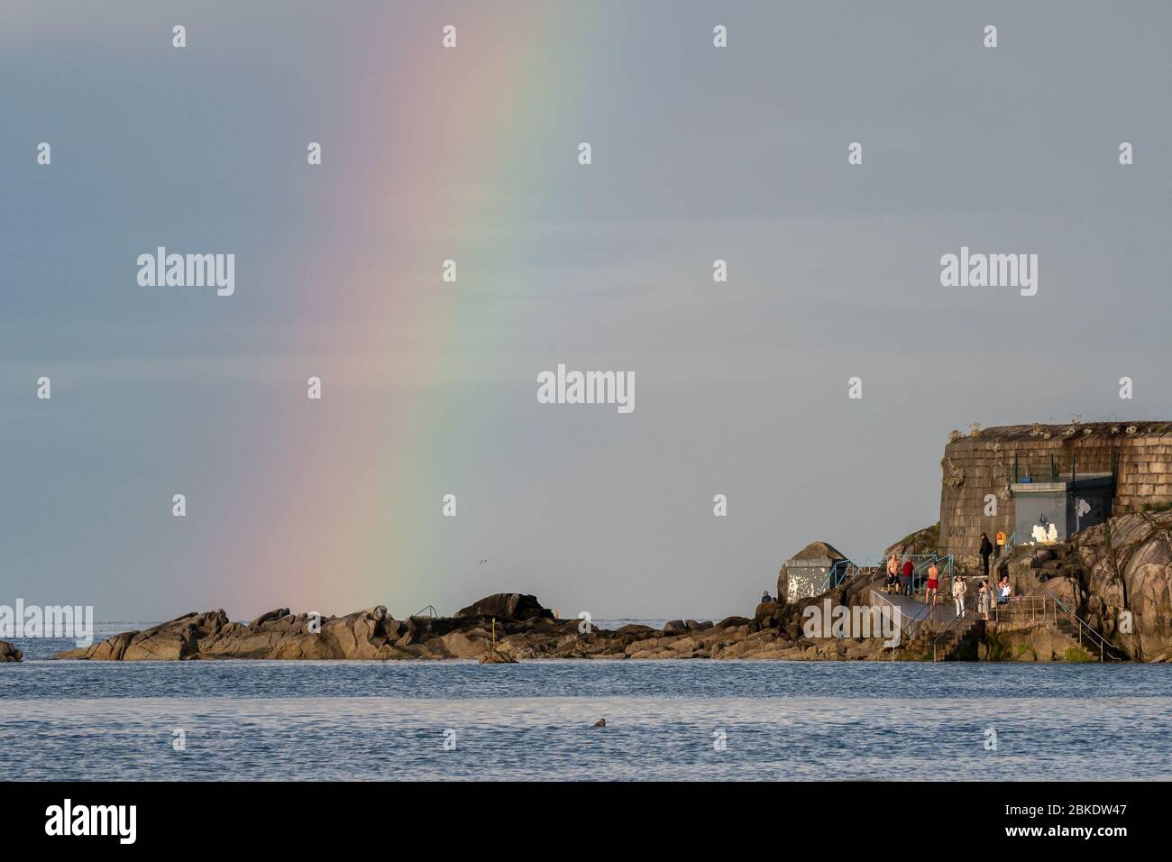 Arcobaleno sopra le rocce e nuotatori che cambiano nel famoso luogo di balneazione a quaranta piedi a Sandycove vicino Dublino in Irlanda Foto Stock