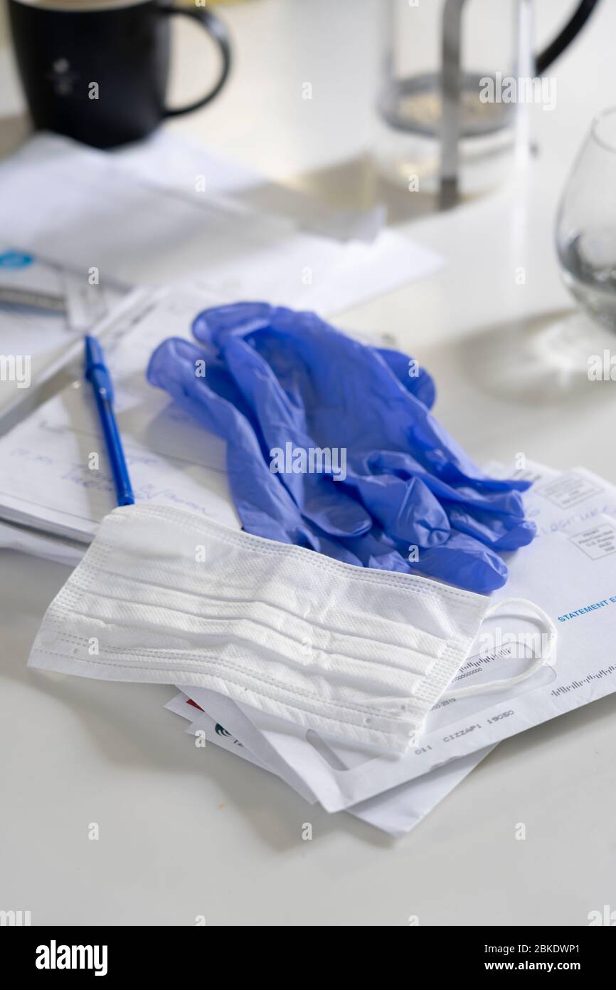Maschera Corona virus con guanti blu su un banco da cucina con una penna e una mail Foto Stock