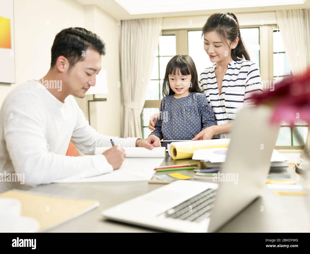 giovane madre asiatica e figlia che guarda padre disegnare un disegno mentre lavora da casa (grafica in background modificata digitalmente) Foto Stock