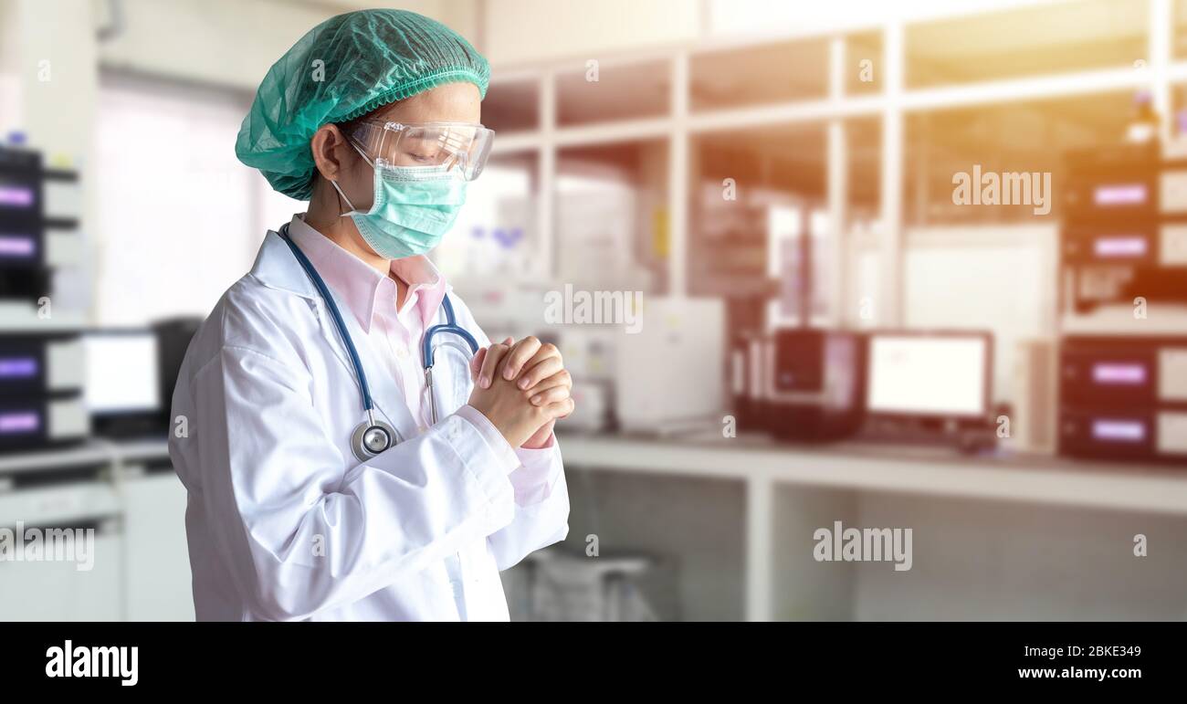 Stress medico asiatico in uniforme, maschera medica e cappuccio fare una preghiera in ospedale durante la trasmissione del Coronavirus Covid-19 focolaio di malattia in situ Foto Stock