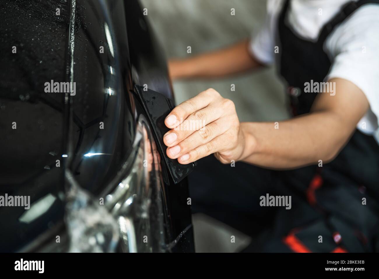 Primo piano di un'auto che avvolge la mano, con un'auto che raddrizza la pellicola trasparente per la protezione con un raschietto per rimuovere le bolle d'aria. Metodo PPF. Foto Stock