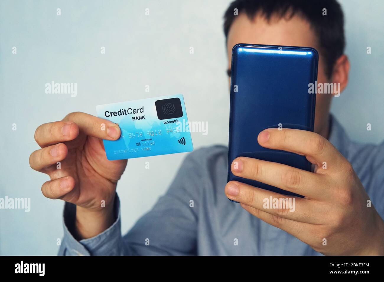 Scatto corto di maschio in camicia che effettua il pagamento online tramite carta di plastica e smartphone. Uomo irriconoscibile che tiene il cellulare e la carta di credito con biometrico Foto Stock