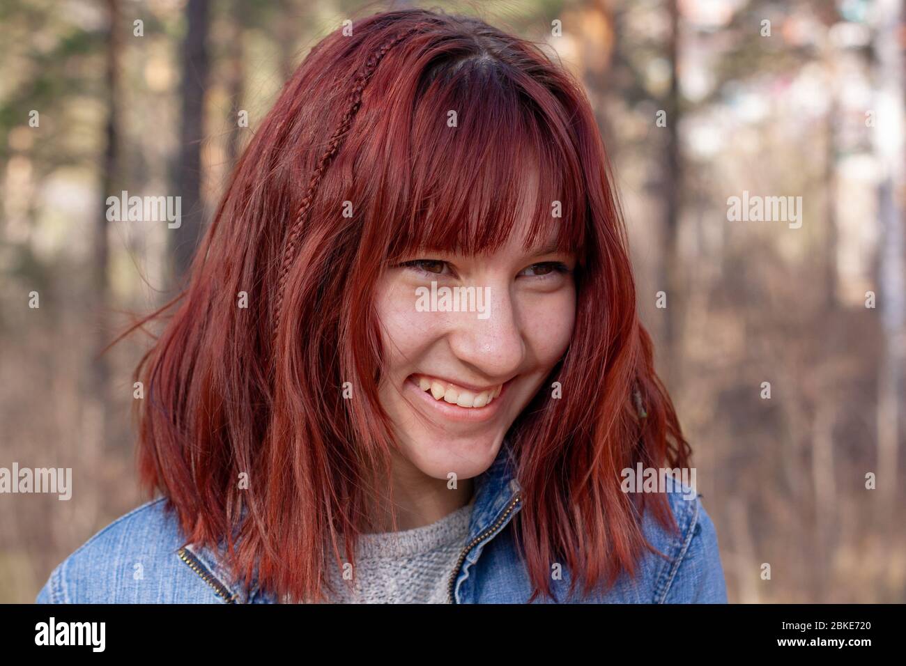 Ritratto di una ragazza ridente di aspetto europeo con capelli rossi. Denti sorridenti e visibili. Guardando lontano. Sfondo sfocato. Orizzontale. Foto Stock