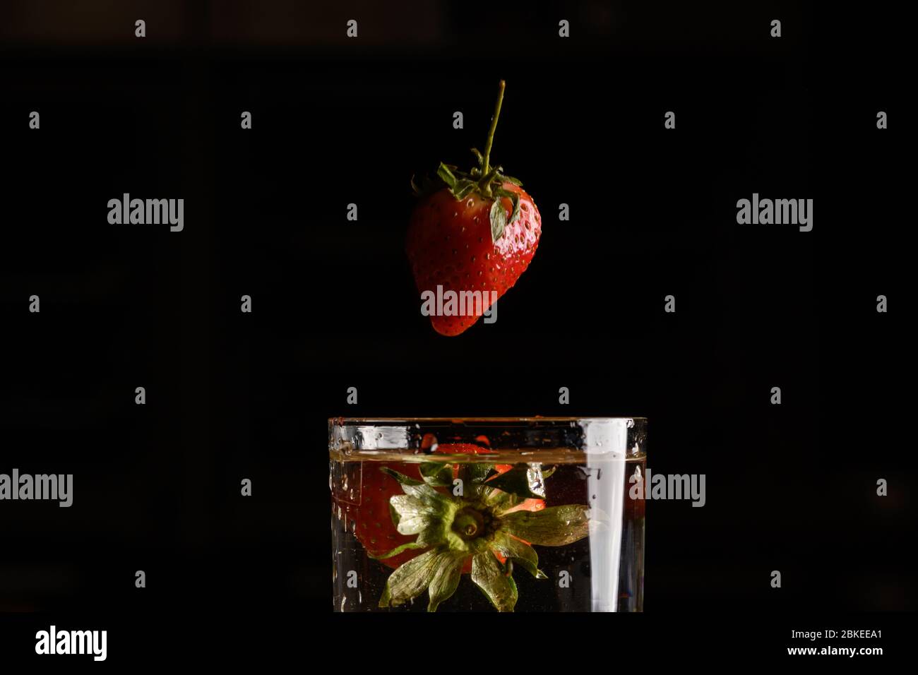Fragola che cade in un bicchiere d'acqua Foto Stock