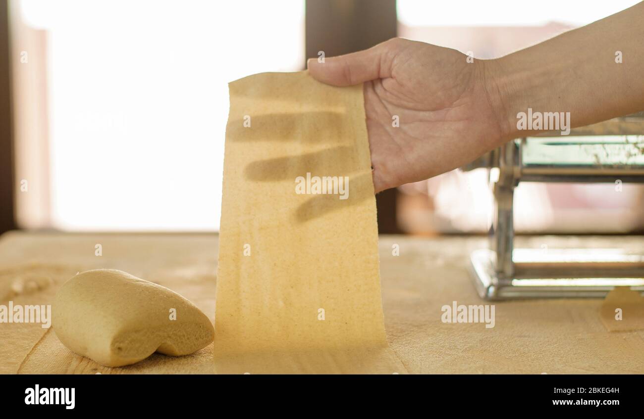 Preparazione della pasta fresca fatta in casa: La mano della donna retroilluminata mostra la trasparenza della pasta fresca appena arrotolata Foto Stock
