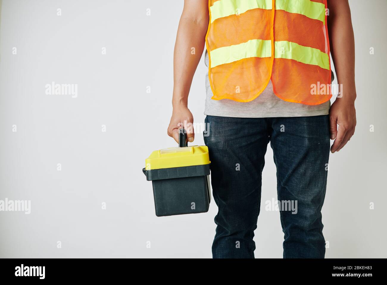 Riparatore in gilet luminoso in piedi con cassetta degli attrezzi contro sfondo grigio chiaro Foto Stock