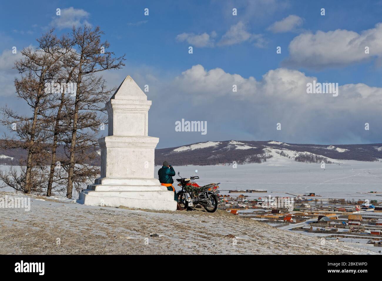 KHATGAL, MONGOLIA, 26 febbraio 2020 : UN uomo in bicicletta guarda la città dalla cima di una collina, vicino ad una colonna bianca. Foto Stock