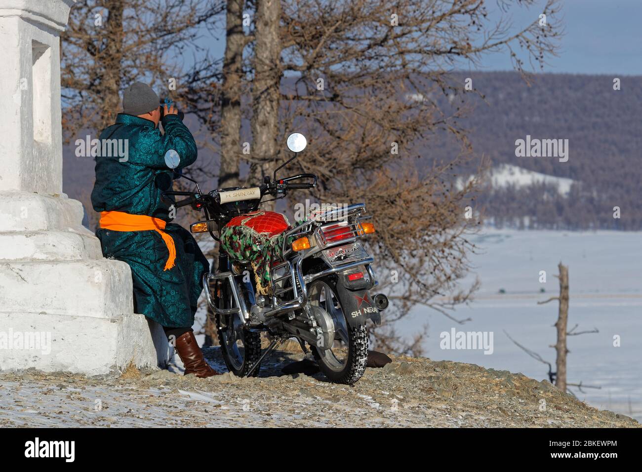 KHATGAL, MONGOLIA, 26 febbraio 2020 : UN uomo in bicicletta guarda la città dalla cima di una collina, vicino ad una colonna bianca. Foto Stock