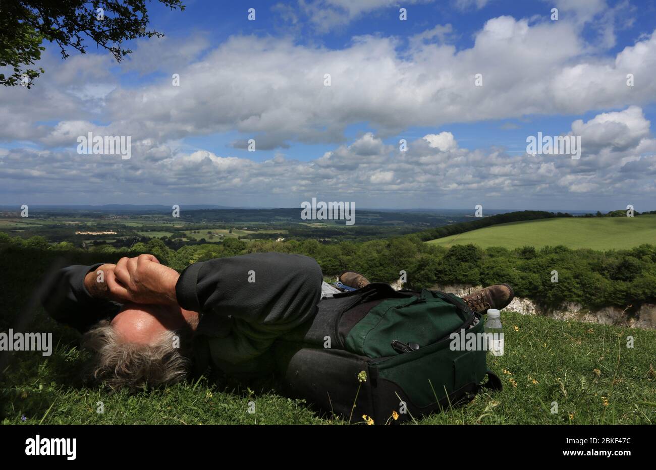 Uomo rilassante al sole estivo, sdraiato sotto un cielo estivo che protegge gli occhi con entrambe le braccia dal sole Foto Stock