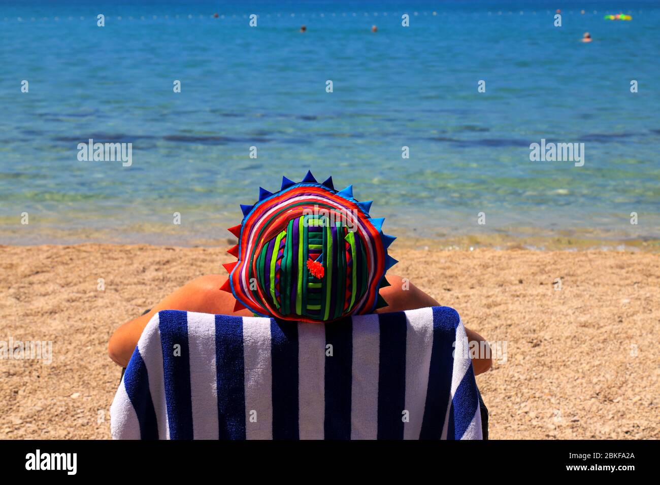 Un uomo in un divertente panama siede in una sedia a sdraio su una spiaggia pulita ed ecologica sotto la Bandiera Blu in Croazia. Vacanze estive vicino mare acqua pulita Foto Stock