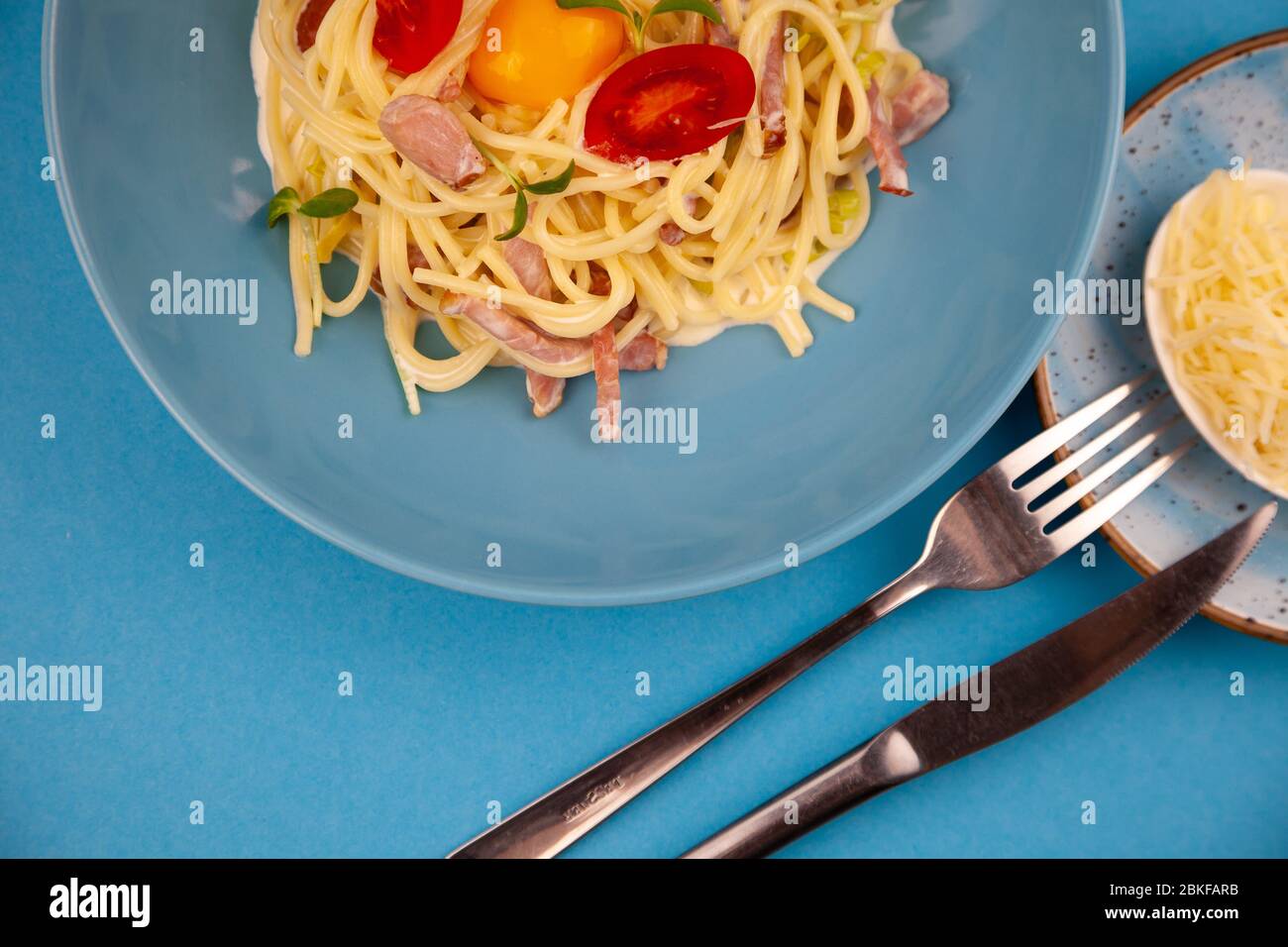 Pasta Carbonara - spaghetti con piccoli pezzi di pancetta, mescolati con salsa di uova, parmigiano. Piastra blu su sfondo blu. Macanons con uovo Foto Stock