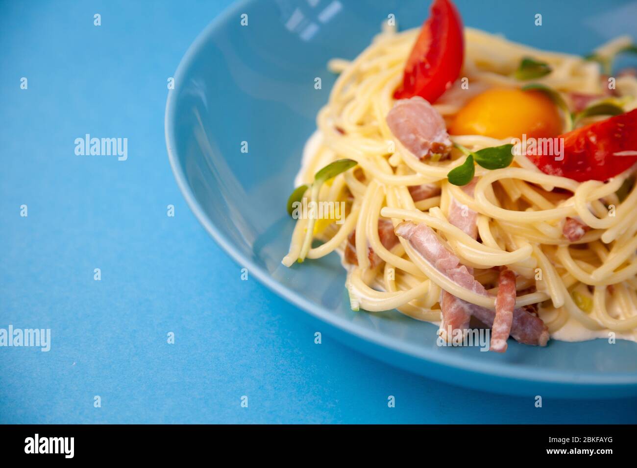Pasta Carbonara - spaghetti con piccoli pezzi di pancetta, mescolati con salsa di uova, parmigiano. Piastra blu su sfondo blu. Macanons con uovo Foto Stock