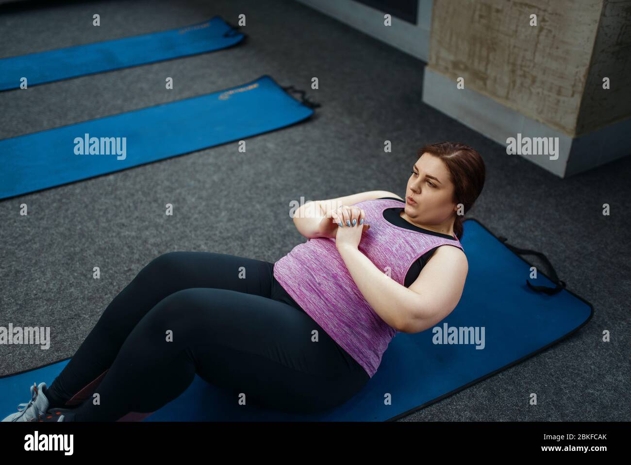 Donna in sovrappeso che fa esercizio sul tappetino in palestra Foto Stock