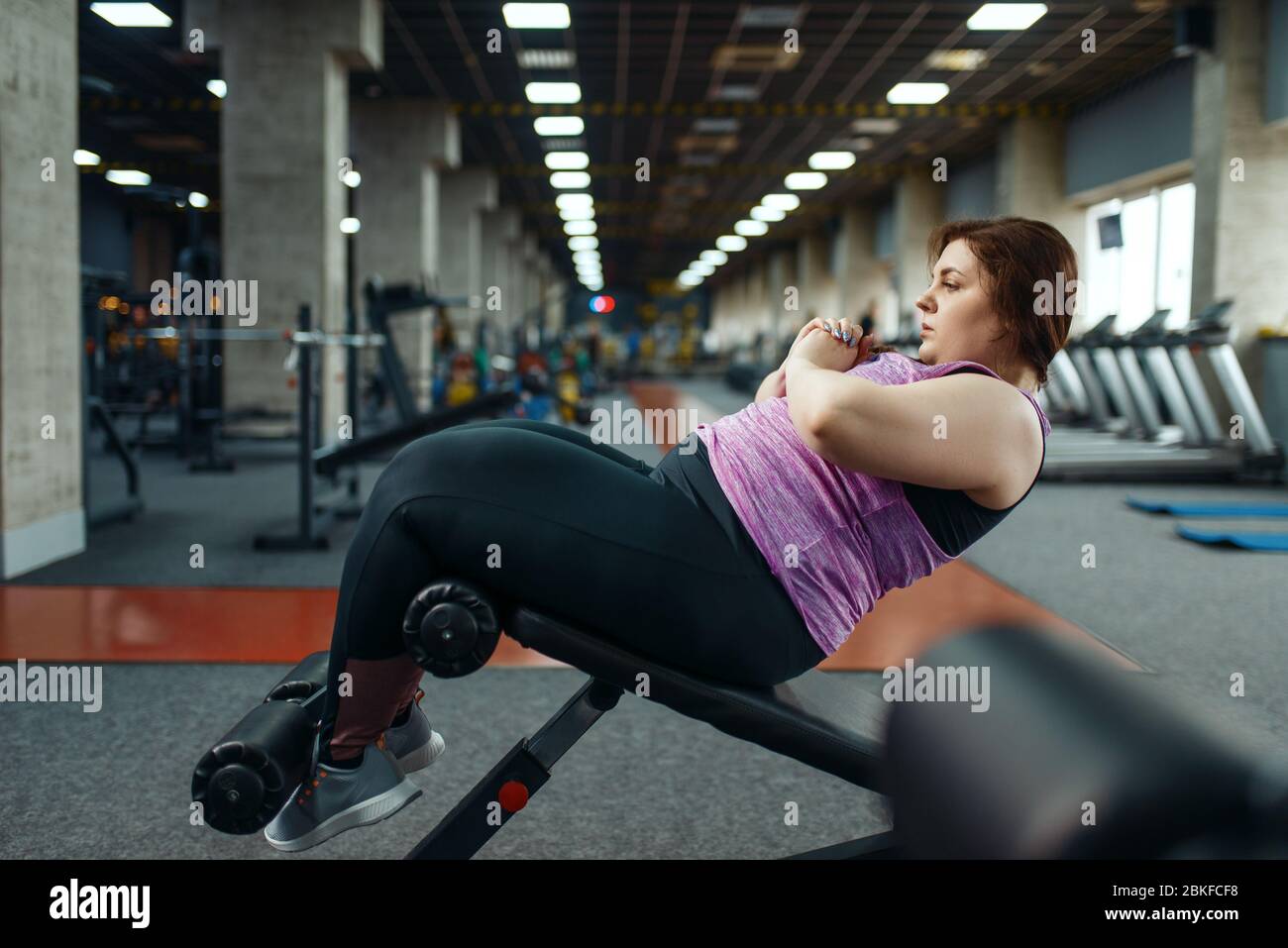 Donna in sovrappeso che fa esercizio su stampa, palestra Foto Stock