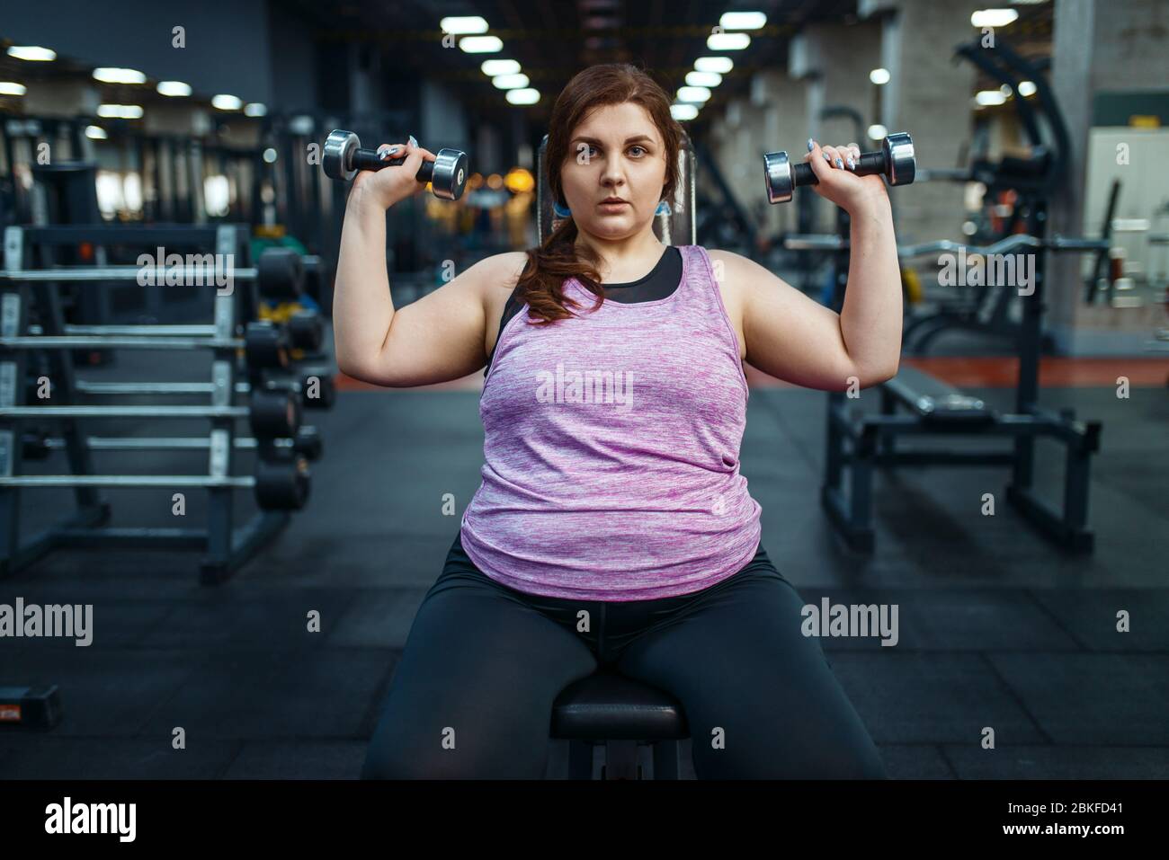 Donna sovrappeso posa con manubri in palestra Foto Stock