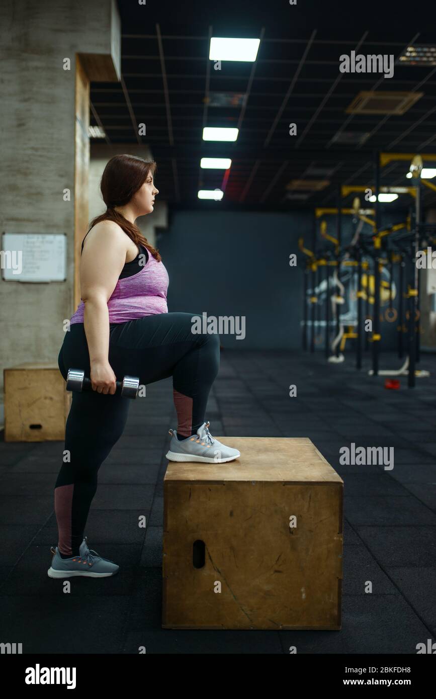 Donna sovrappeso con manubri in palestra, vista laterale Foto Stock