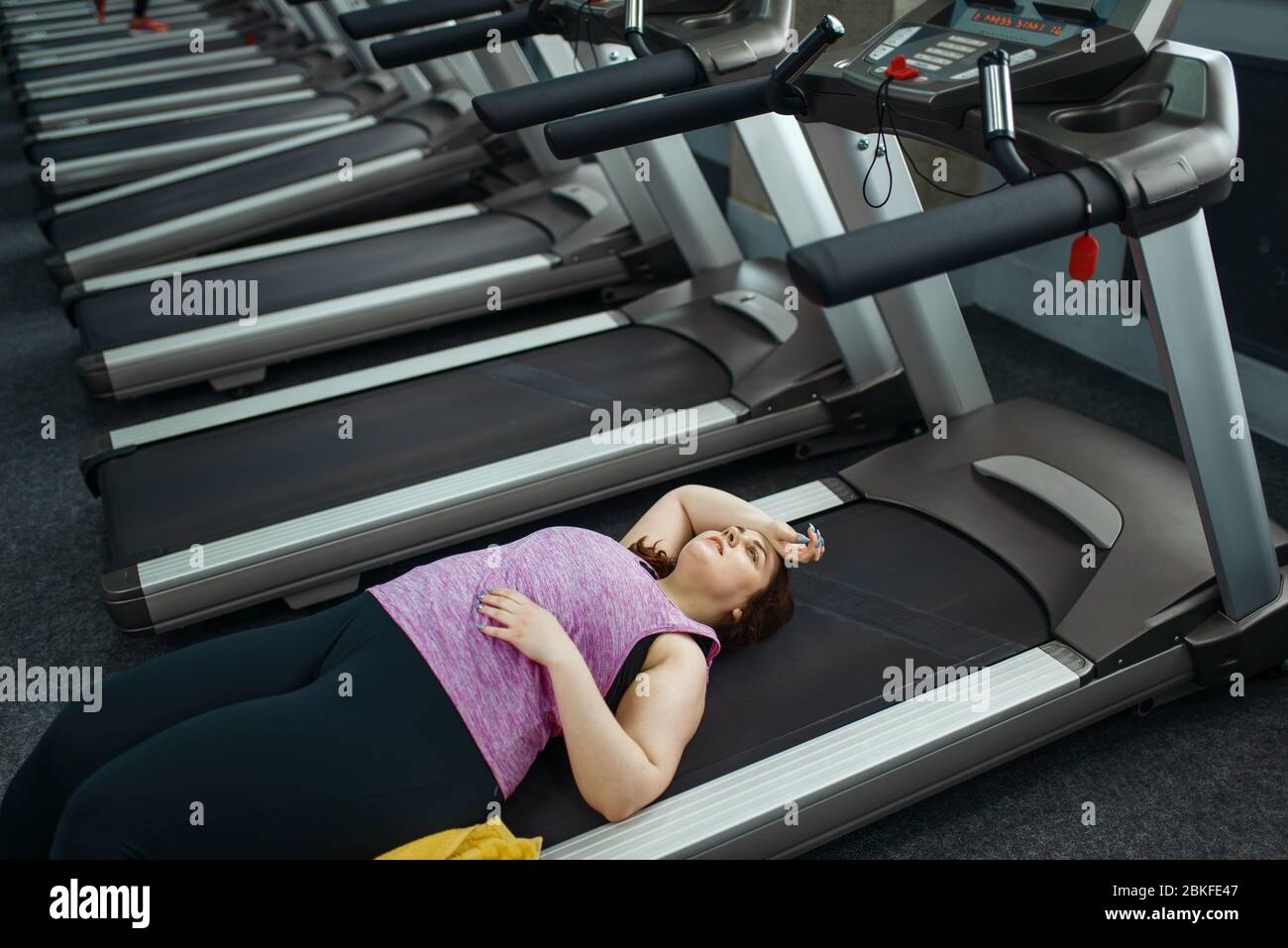 Donna stanca sovrappeso sdraiata sul tapis roulant in palestra Foto Stock