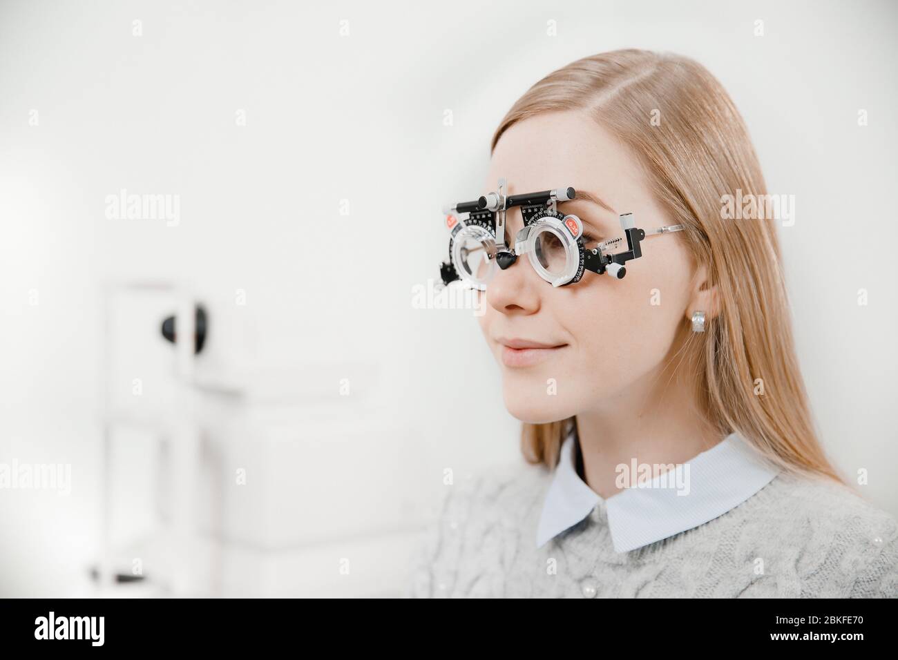 Ritratto di tre quarti bionda bella ragazza giovane con sorriso leggero in occhiali speciali oftalmici per il controllo visivo e la selezione delle lenti Foto Stock