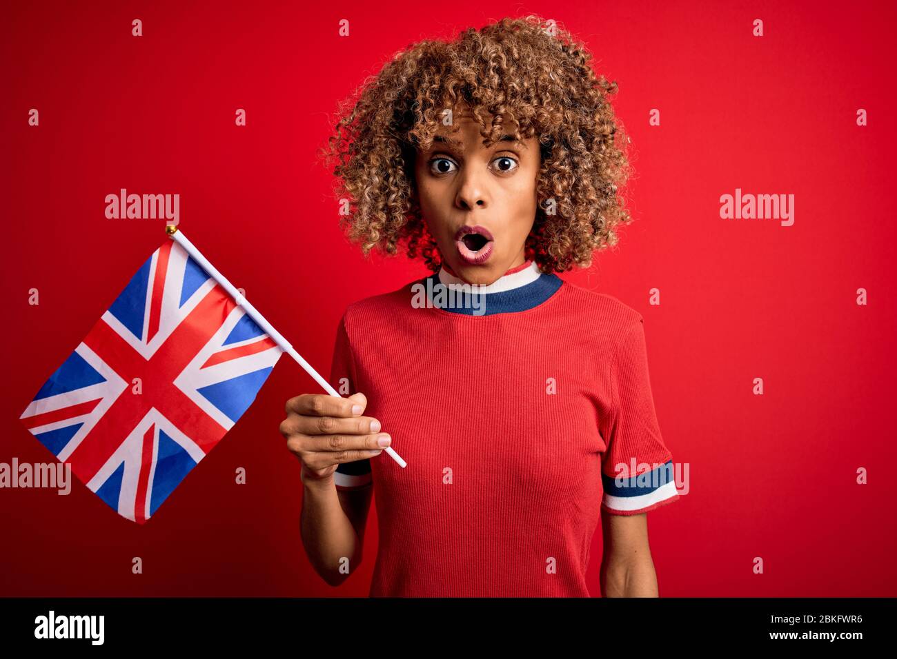 Giovane maledetta afro-americana che tiene la bandiera britannica per celebrare il referendum sulla brexit spaventata in uno shock con un volto a sorpresa, impaurita ed eccitata dalla paura ex Foto Stock