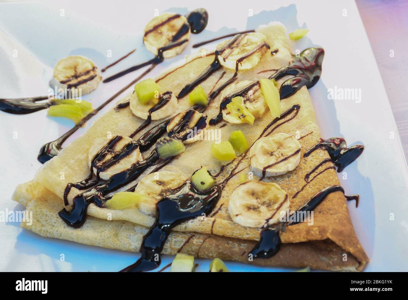 Tradizionale frittella ripiegata triangoli con salsa al cioccolato e condimenti di frutta durante il festival del cibo di strada. Servito su un piatto bianco Foto Stock