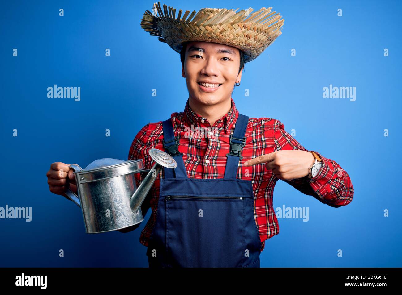 Giovane bel contadino cinese uomo che indossa grembiule e cappello di paglia  che tiene annaffiatura può con la faccia sorpresa che punta il dito a se  stesso Foto stock - Alamy