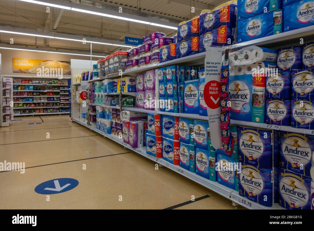 Scaffali finalmente pieni di rotolo di gabinetto alla fine di una giornata nel supermercato Tesco mostrando due metri di distanza sociale marcatori e un senso freccia sistema su t. Foto Stock