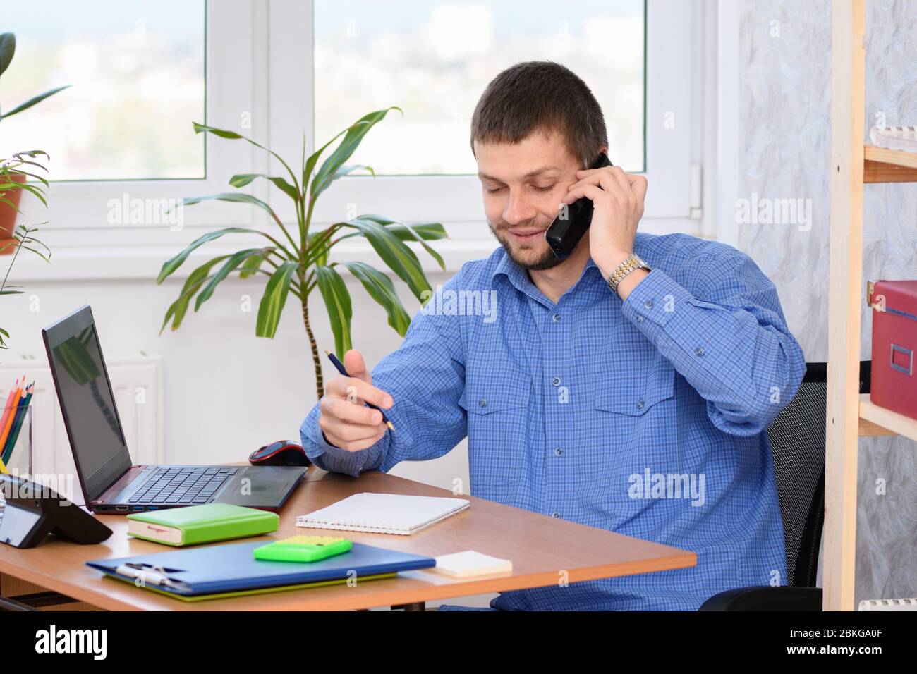 Specialista di ufficio che parla al telefono e prende appunti in un notebook Foto Stock