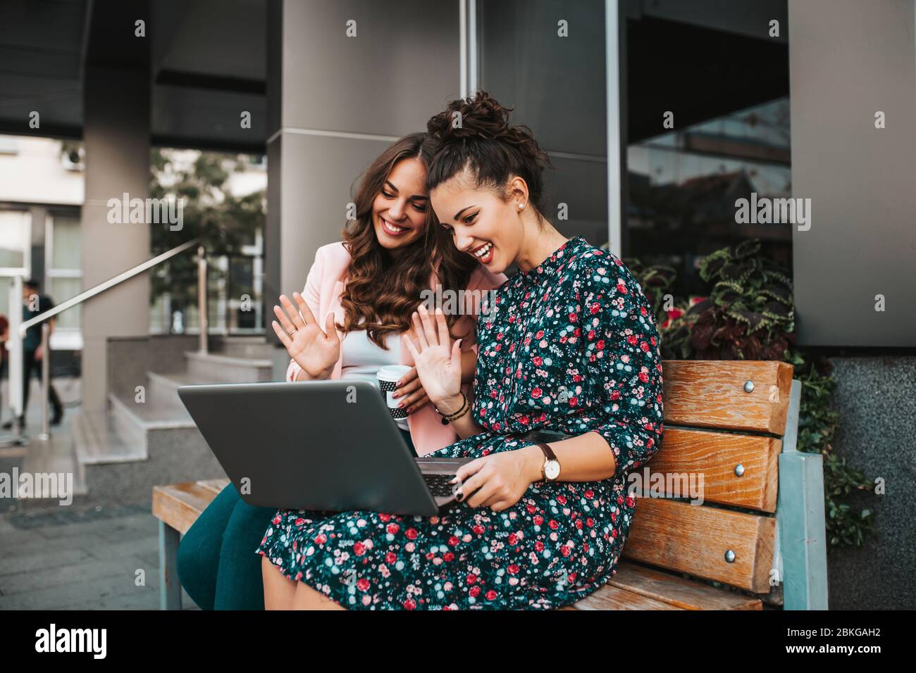 Due belle giovani donne che si muovono mano e parlano mentre si videochiama con i propri amici su un computer portatile in una strada della città. Foto Stock