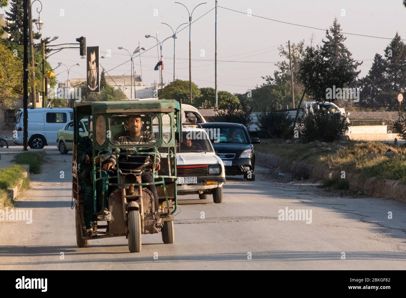 Un tuk-tuk per le strade con un ritratto di Bashar al-Assad sullo sfondo, Qamishli, Siria. Foto Stock