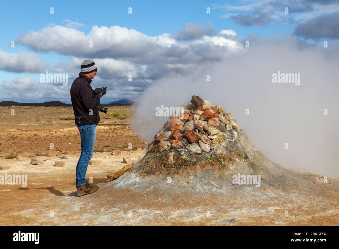 Un visitatore che si trova accanto ad un mucchio di pietre sopra una bocca di vapore nella zona geotermica di Námafjall (chiamata anche Hverir), Islanda. Foto Stock