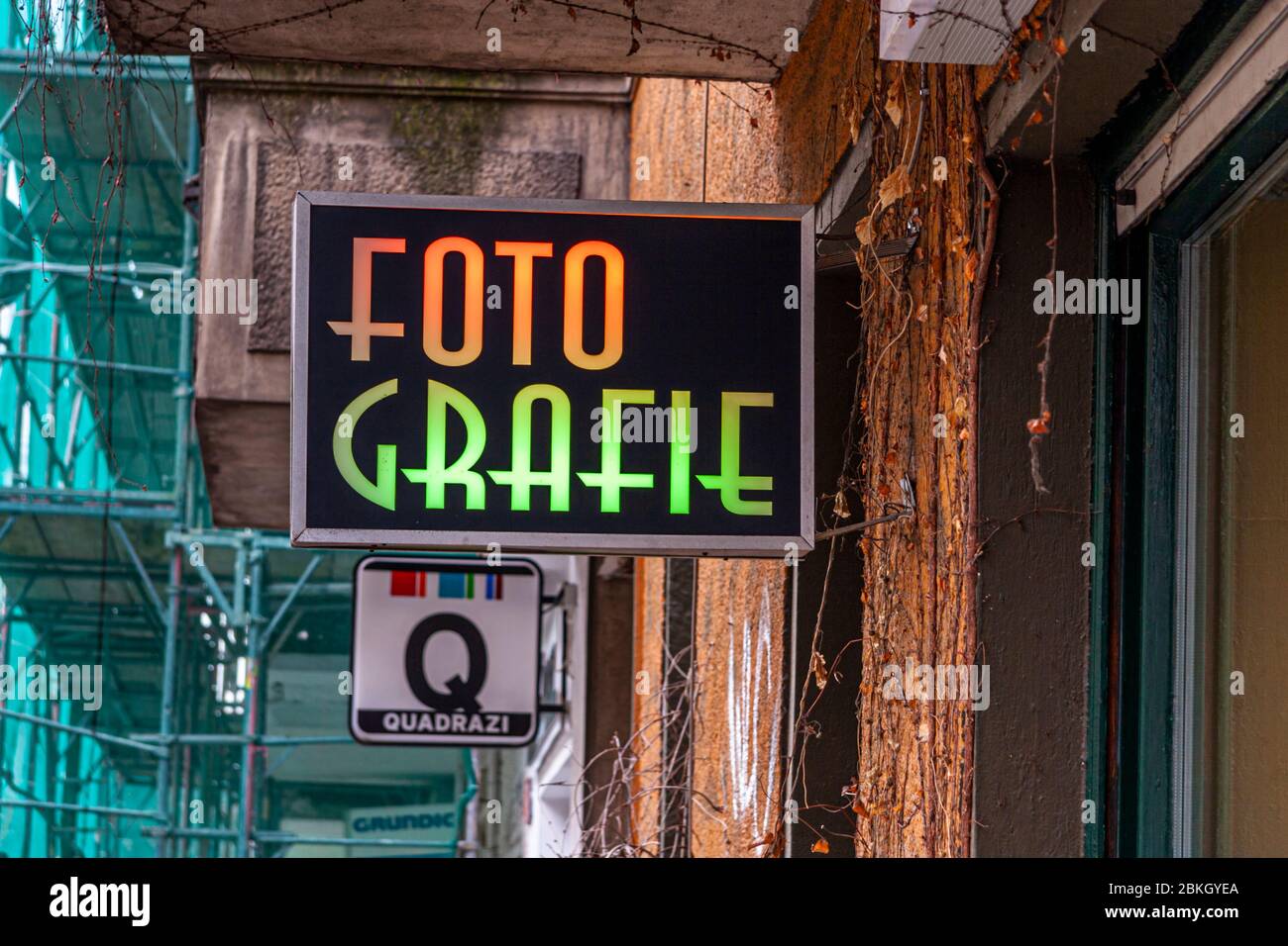 Un cartello illuminato bicolore con le parole "Foto Grafie" è appeso sotto un ponteggio su una facciata di edificio ricoperta di edera; sotto di esso è montato un cartello pubblicitario rotondo. Unter den Linden, Friedrichswerder, Dorotheenstadt, Berlino, 10117, Germania Foto Stock