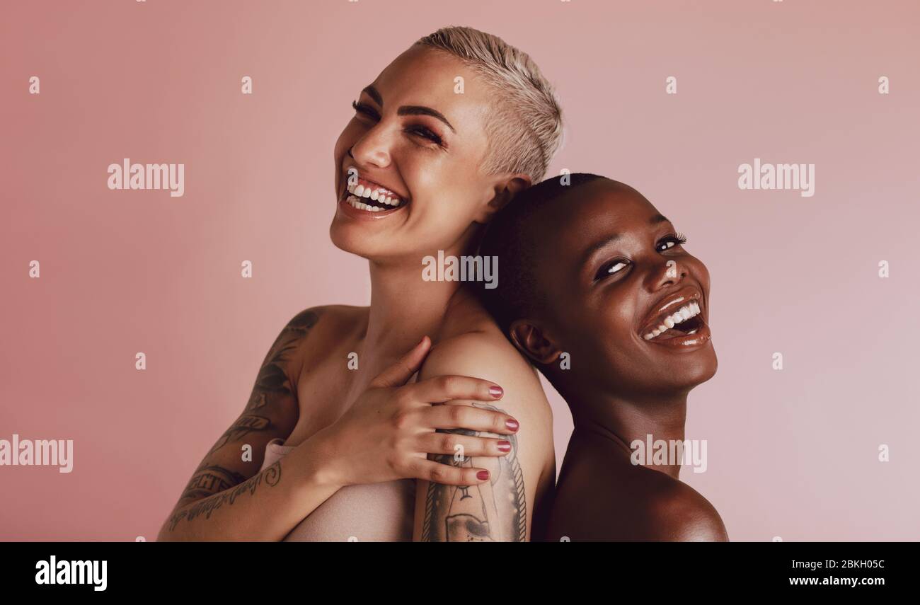 Due donne con capelli dal taglio brusio che si alzano indietro e sorridono alla fotocamera. Modelli femminili con bella pelle sorridente insieme su backgroun beige Foto Stock