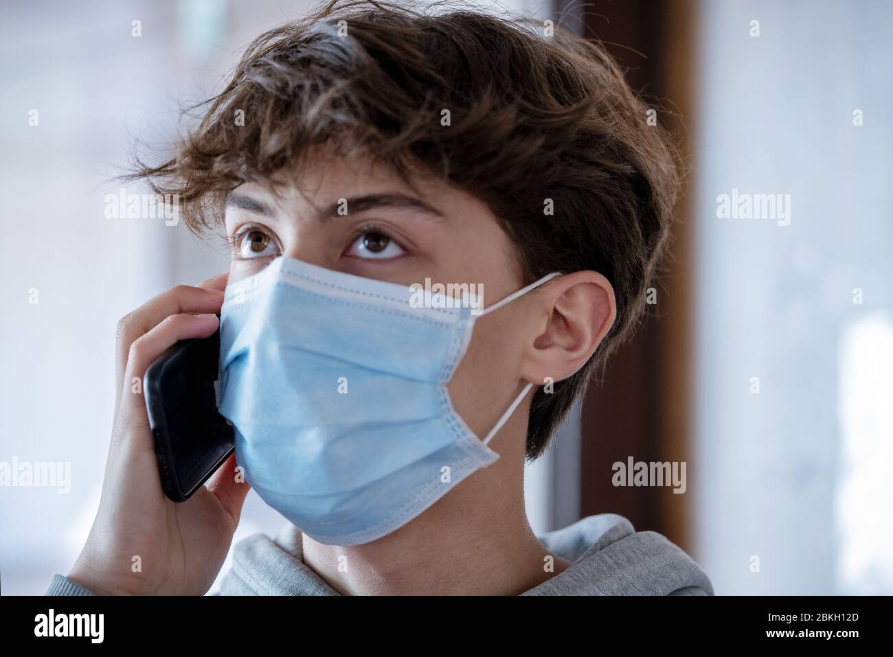 Primo piano di un ragazzo adolescente con maschera medica che parla sullo smartphone durante il blocco Foto Stock