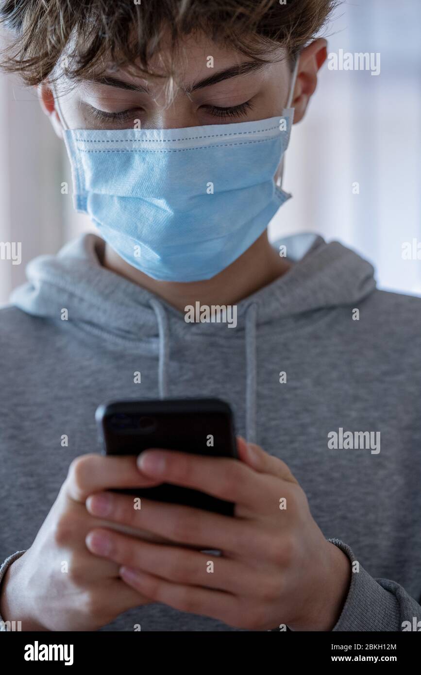 Primo piano di un adolescente con maschera medica utilizzando lo smartphone durante il coronavirus Foto Stock