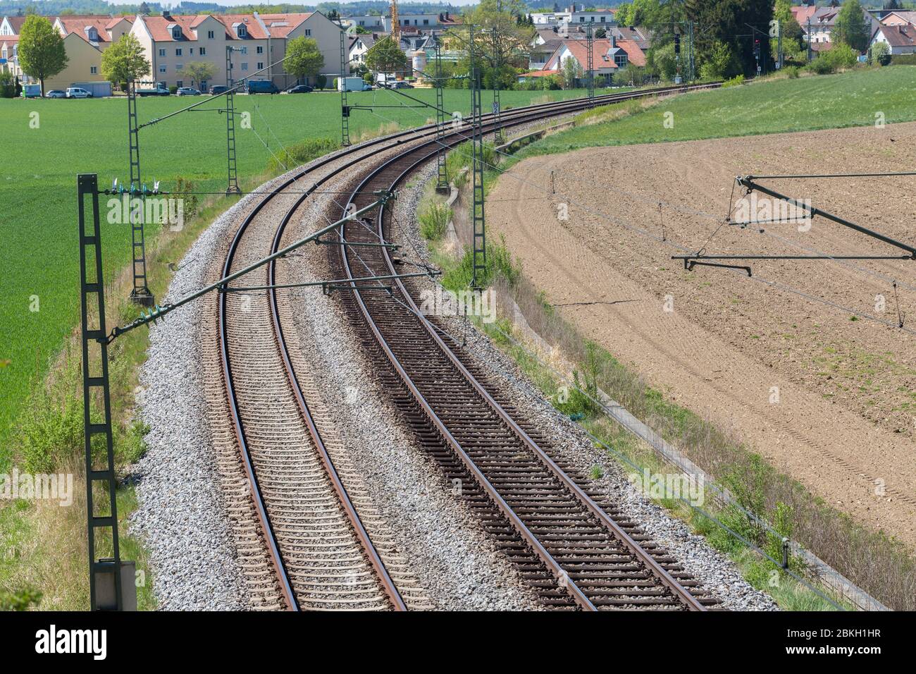 Due binari ferroviari che conducono attraverso un paesaggio con campi verdi e marroni. Una città all'orizzonte. Con piegatura / curva. Simbolo di viaggio, viaggio. Foto Stock