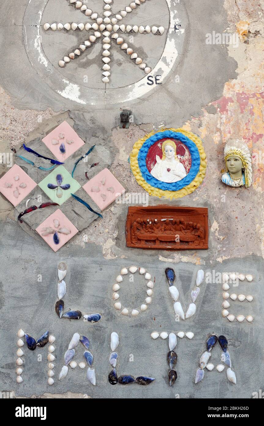 Particolare di un'installazione artistica sulla parete di un edificio nel villaggio di Marsaxlokk, Malta. I materiali intarsiati includono gusci e piastrelle. Foto Stock