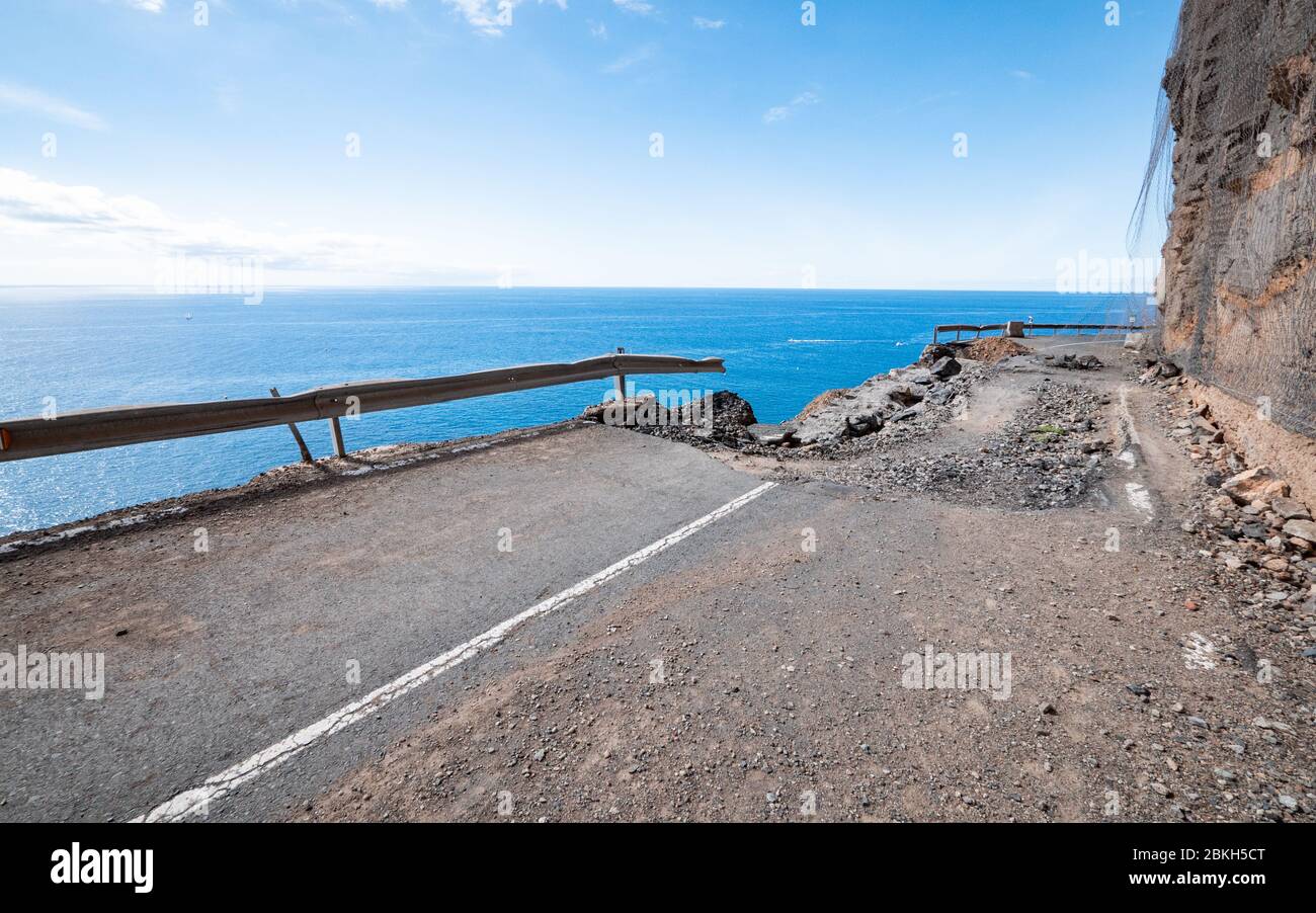 Danni alla strada laterale della scogliera e erosione costiera. Effetti ambientali su una strada nell'isola delle Canarie di Gran Canaria. Foto Stock