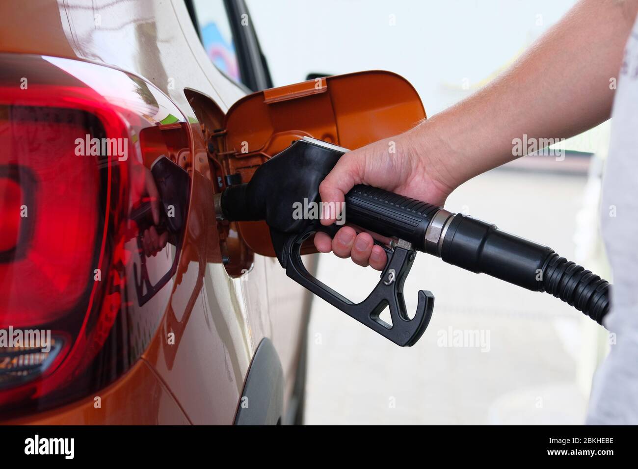 L'uomo riempie la sua auto arancione con una benzina al distributore di benzina. Pompa della stazione di servizio. Per riempire la vettura con carburante. Foto Stock