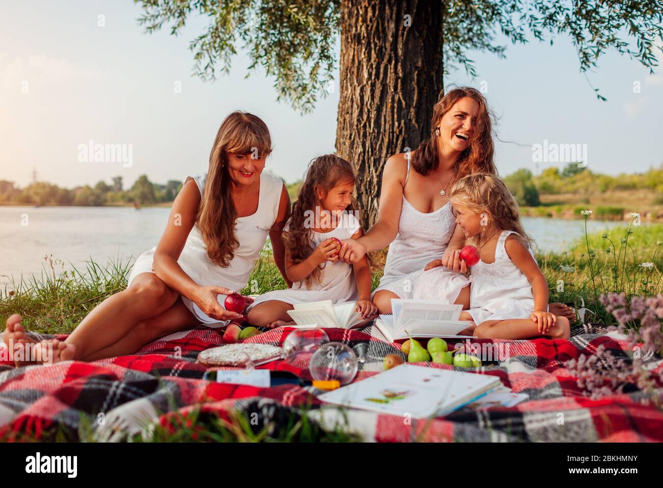 Giorno della madre. Famiglia che ha pic-nic in primavera fiume al tramonto. Madre, nonna e bambini ridono. Foto Stock
