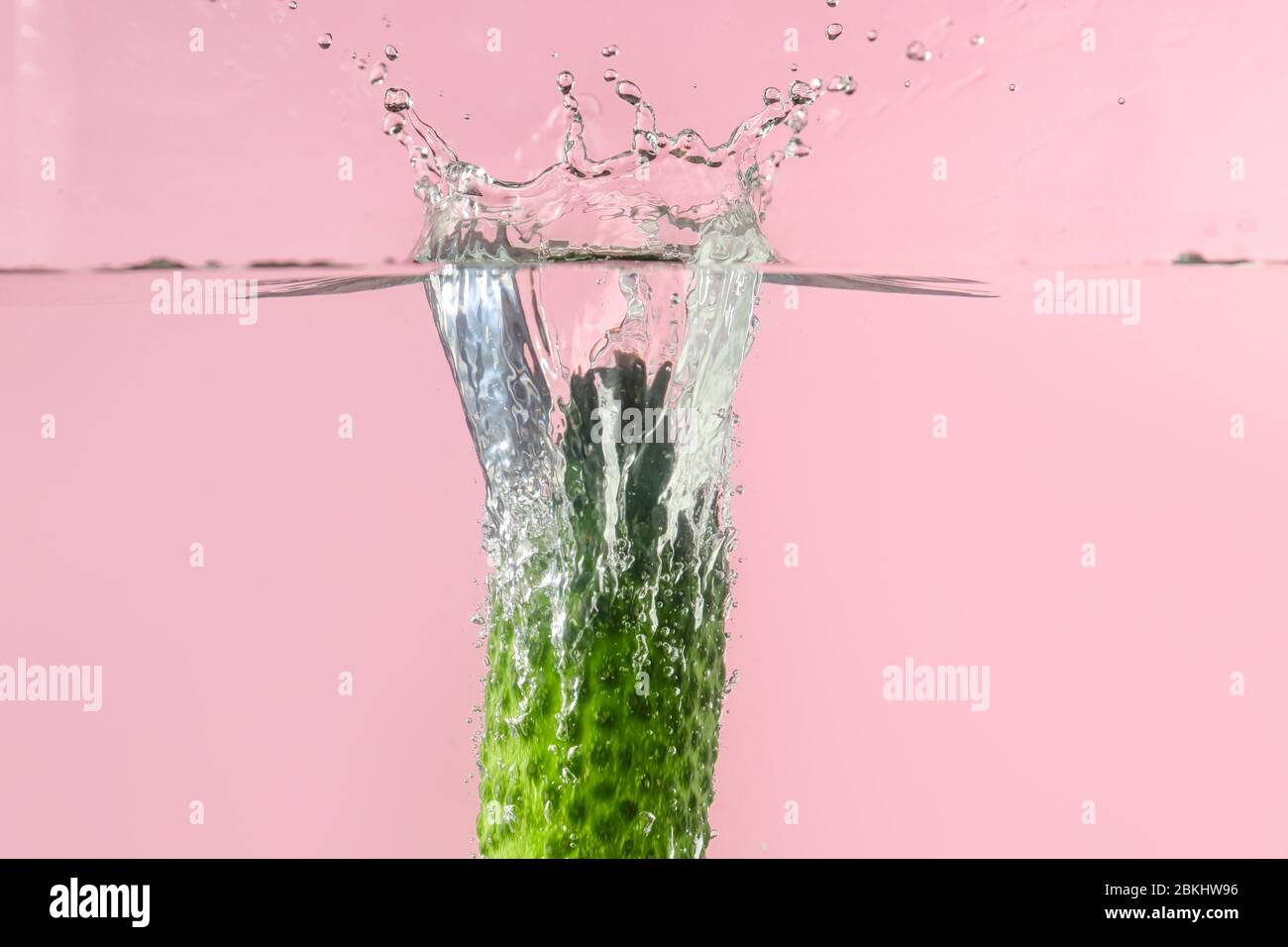 Caduta di cetrioli freschi in acqua contro sfondo colore Foto Stock