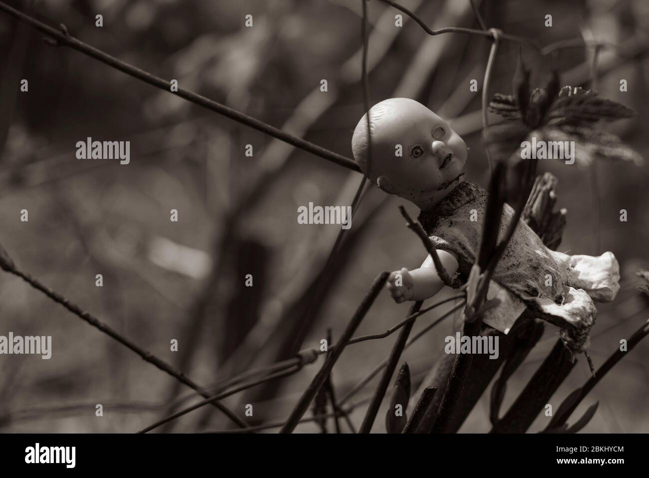 Una vecchia bambola sporca si appende su un recinto, bambola del bambino con un solo occhio, bambola creepy, foto in bianco e nero, seppia Foto Stock